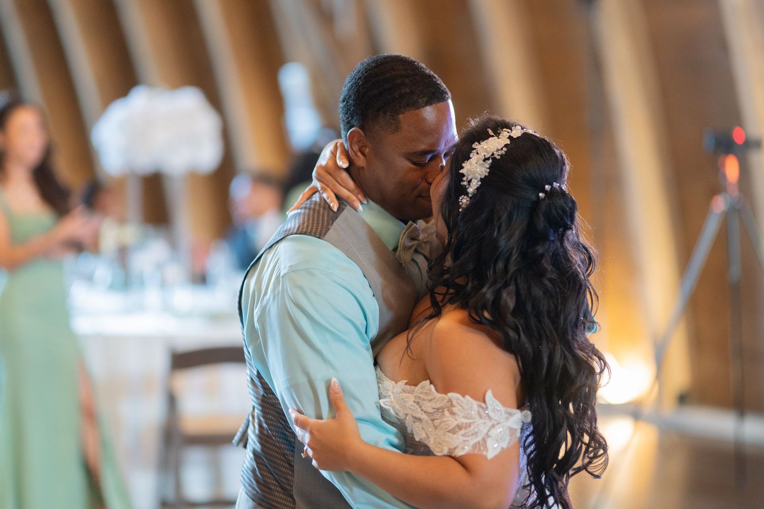 A couple shares their first dance kiss at a wedding reception in an elegant venue with warm lighting.