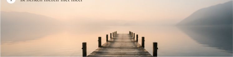 A serene wooden dock extends over a calm misty lake surrounded by mountains in soft morning light.