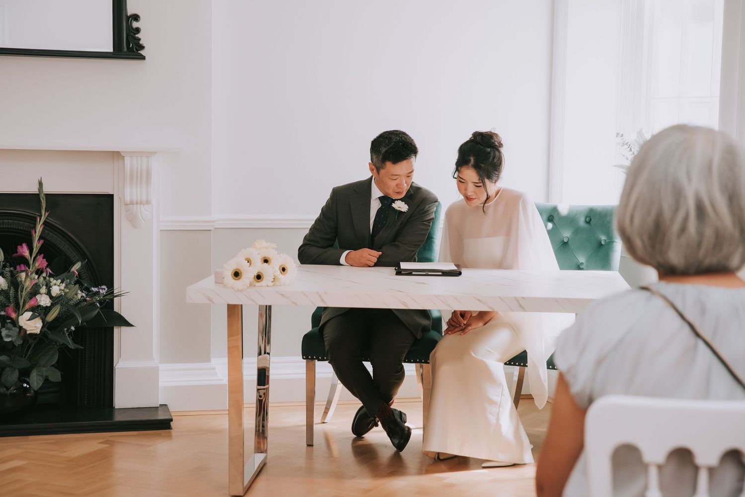 Bride and groom signing wedding register at white table during intimate civil ceremony.