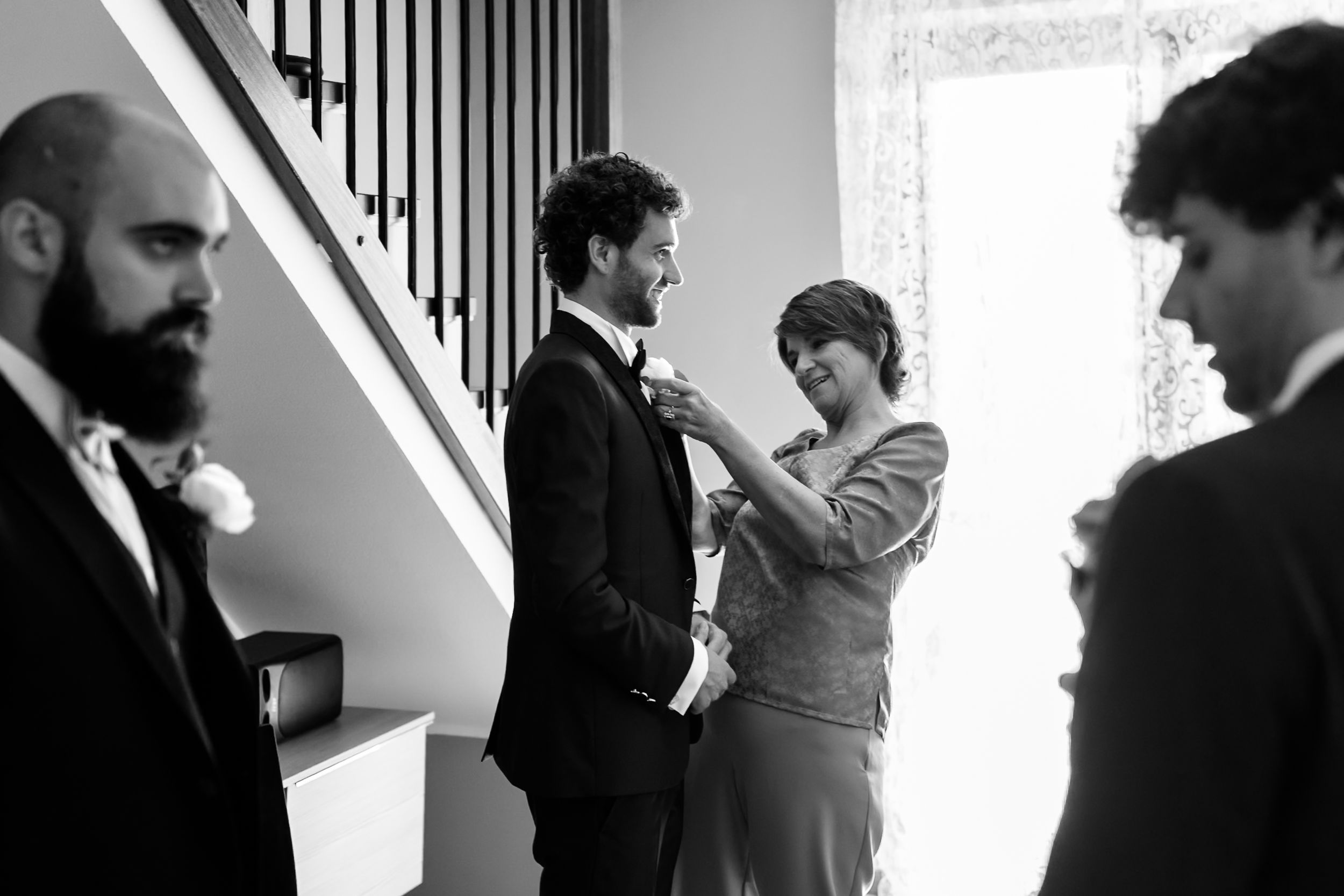 Black and white photo of a woman pinning a boutonniere on a groom in a tuxedo before his wedding ceremony.