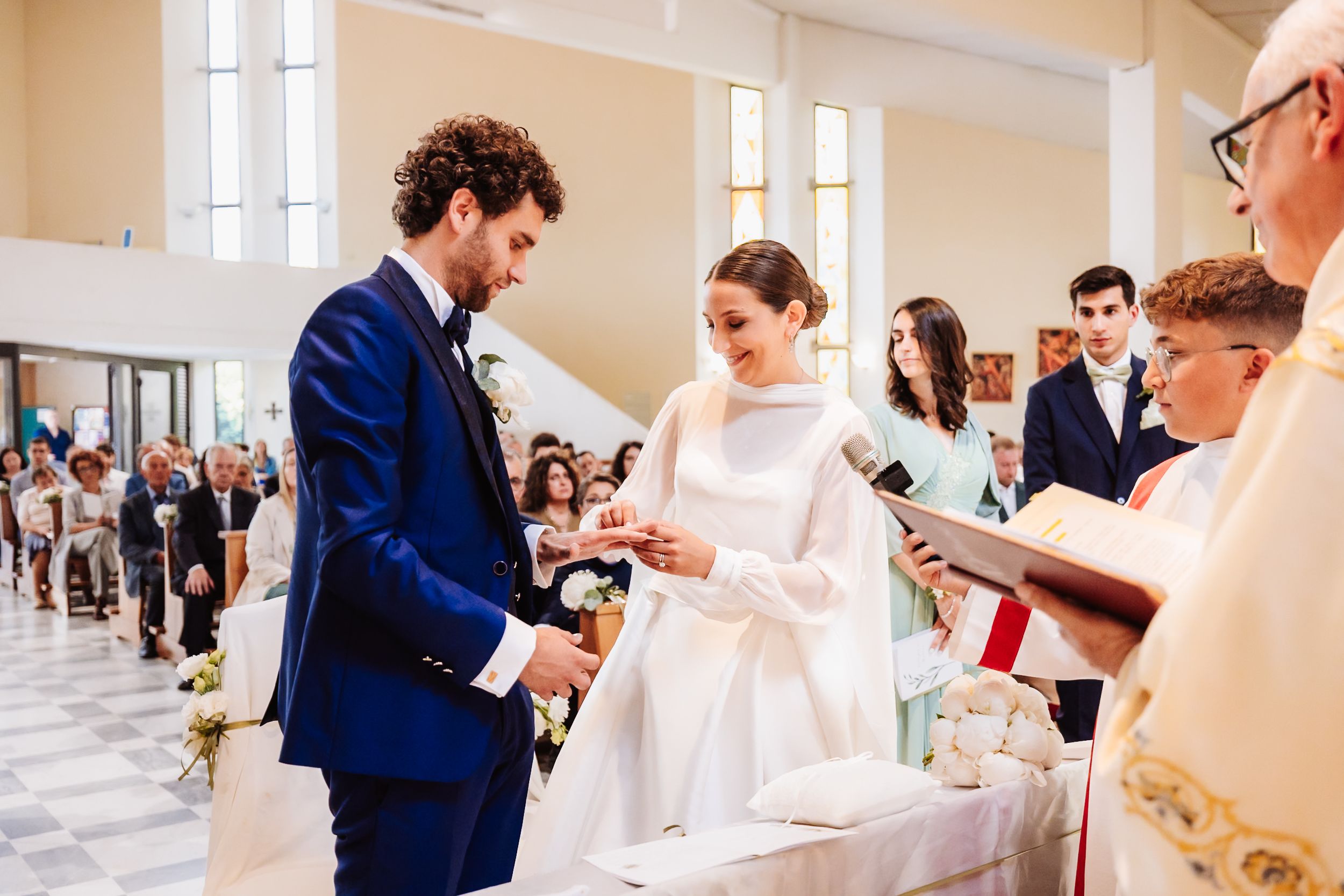Bride and groom exchanging rings during a church wedding ceremony, officiated by a priest.