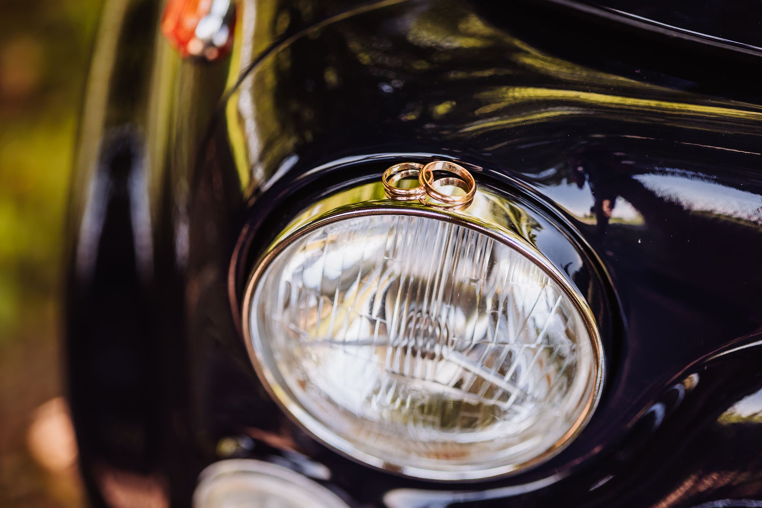Two gold wedding rings resting on the headlight of a vintage black classic car.