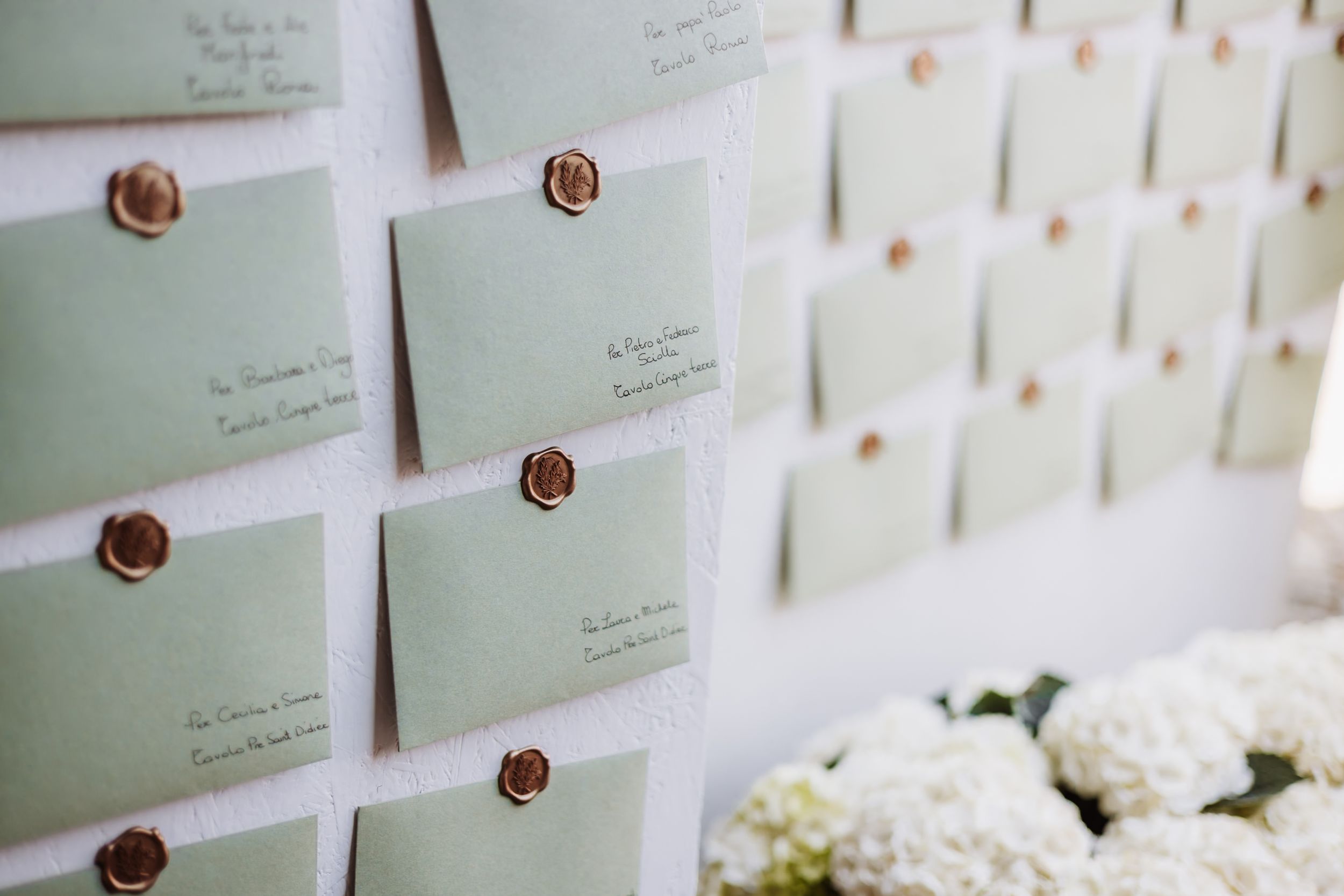 Elegant sage green escort cards with gold wax seals displayed on a white board at a wedding reception.
