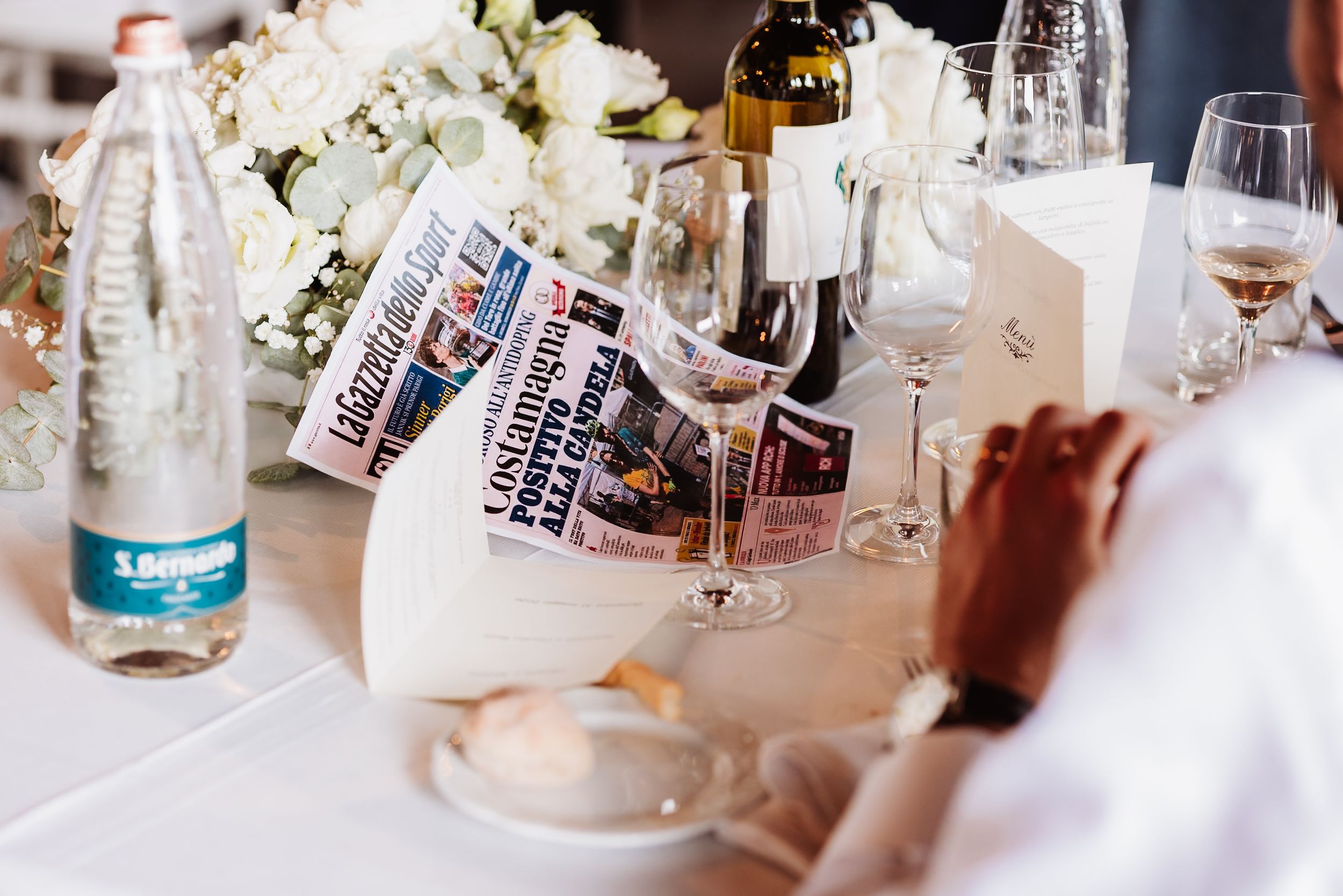 Elegant wedding table setting with wine glasses, water bottle, flowers, and newspapers as decorative elements.