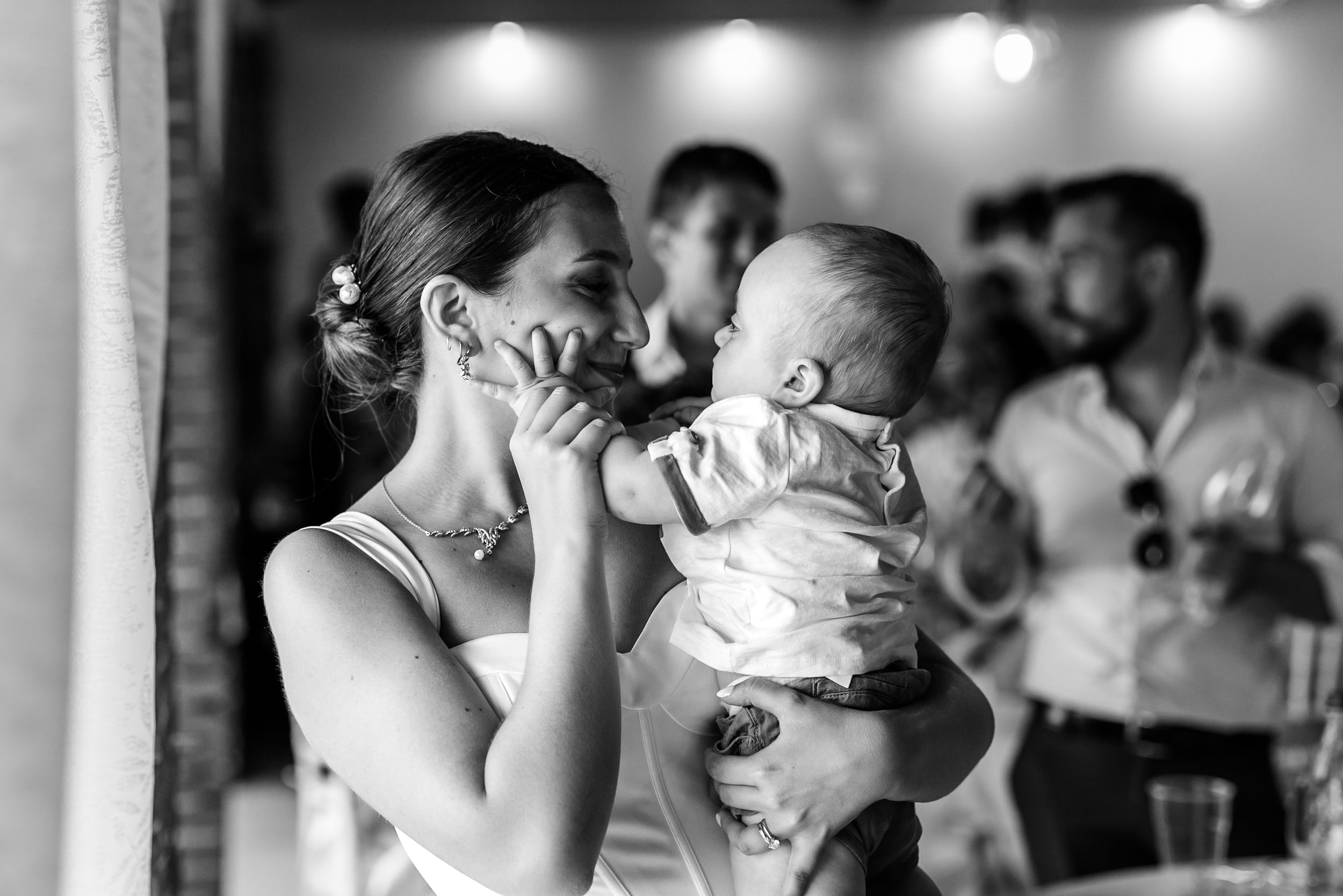 Black and white photo of a smiling bride holding a baby at a wedding reception.