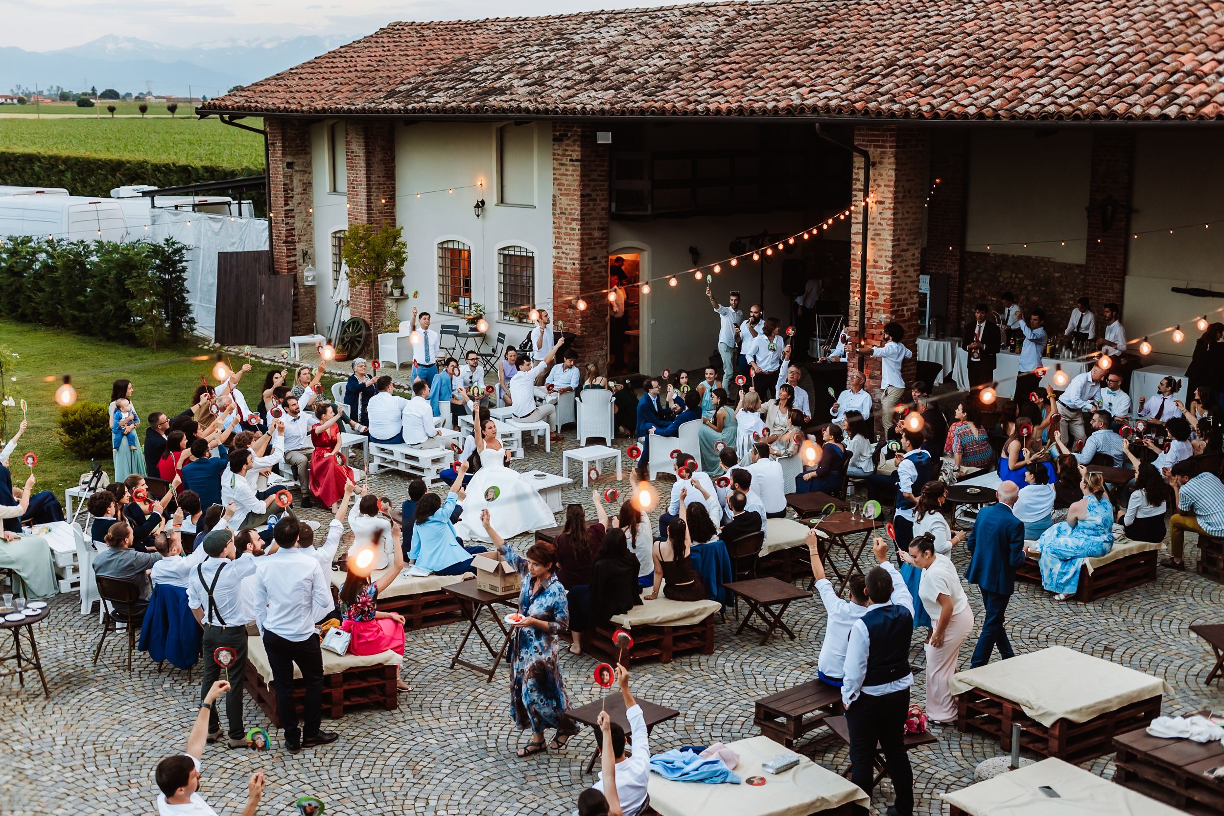 Aerial view of an elegant outdoor wedding reception at a rustic Italian villa with string lights and guests.