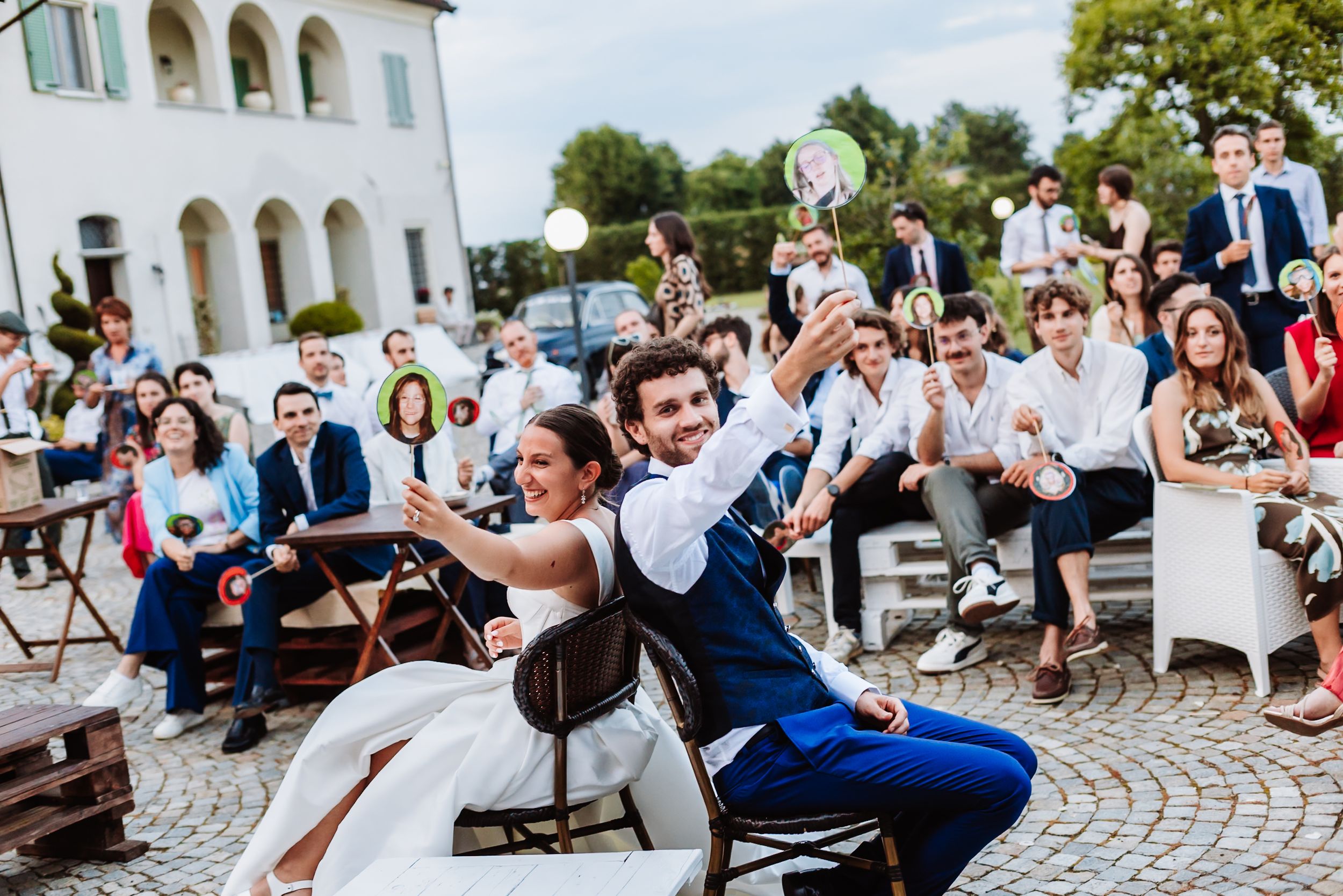 Bride and groom celebrate outdoors at wedding reception with cheering guests seated behind them.