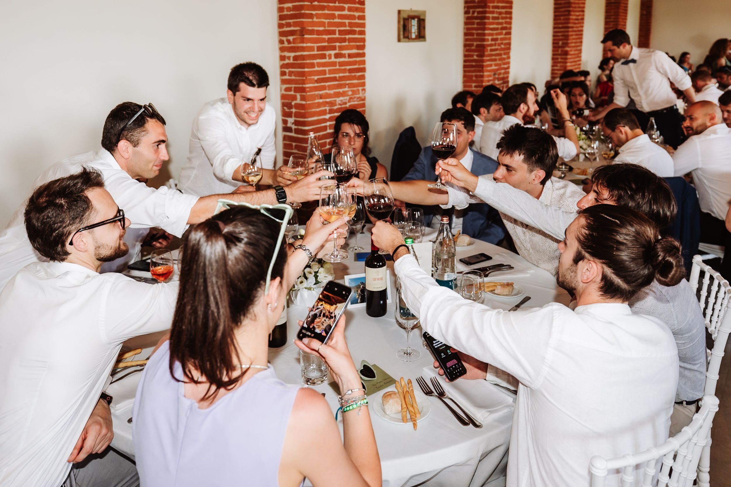 Group of guests in white attire toasting drinks together at a festive wedding reception dinner table.