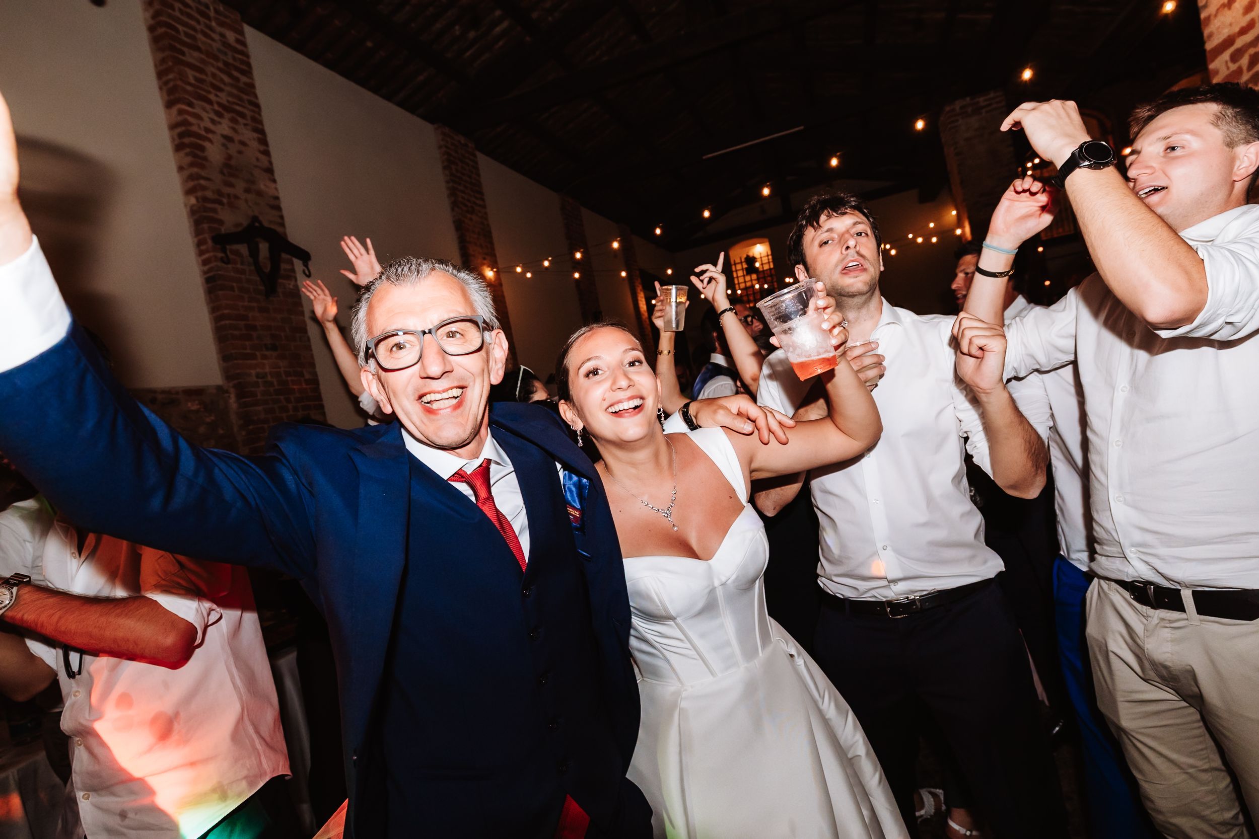 Bride and groom celebrating joyfully on the dance floor with guests at a lively indoor wedding reception.