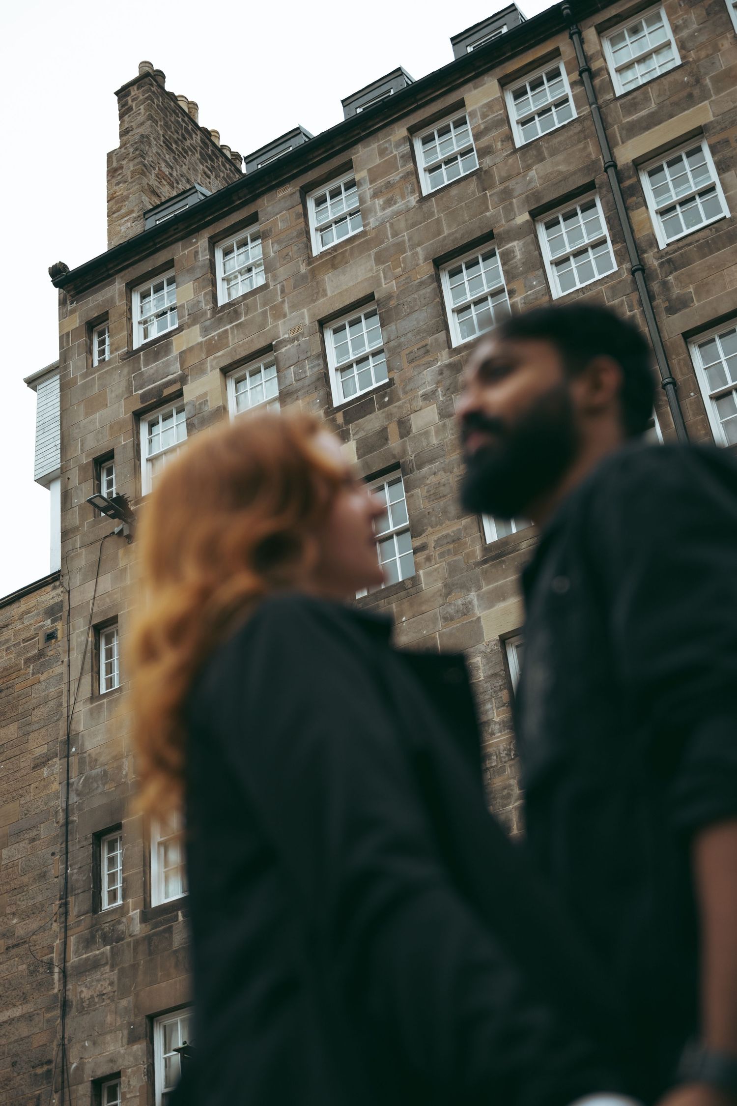 Couple in black jackets standing before historic stone building in Edinburgh.