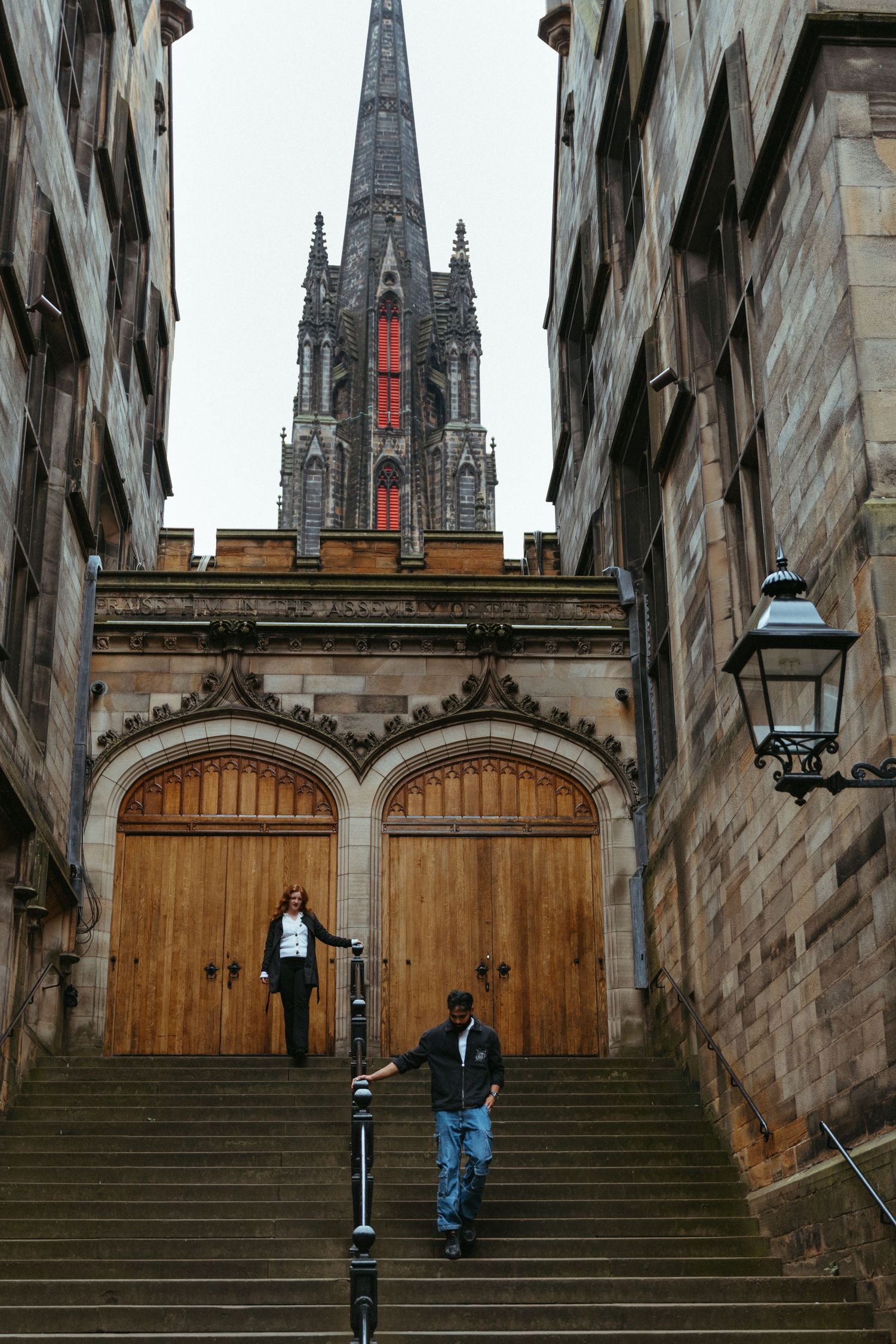 Couple on stone steps leading to Gothic church entrance with tall spire above.