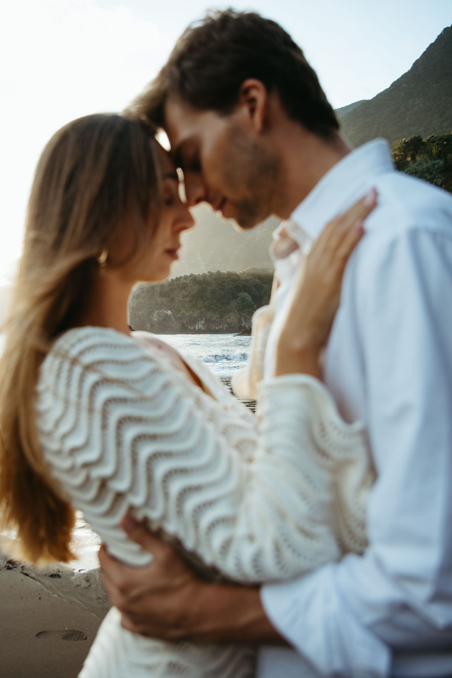 Couple embracing forehead to forehead at golden hour on scenic ocean beach.