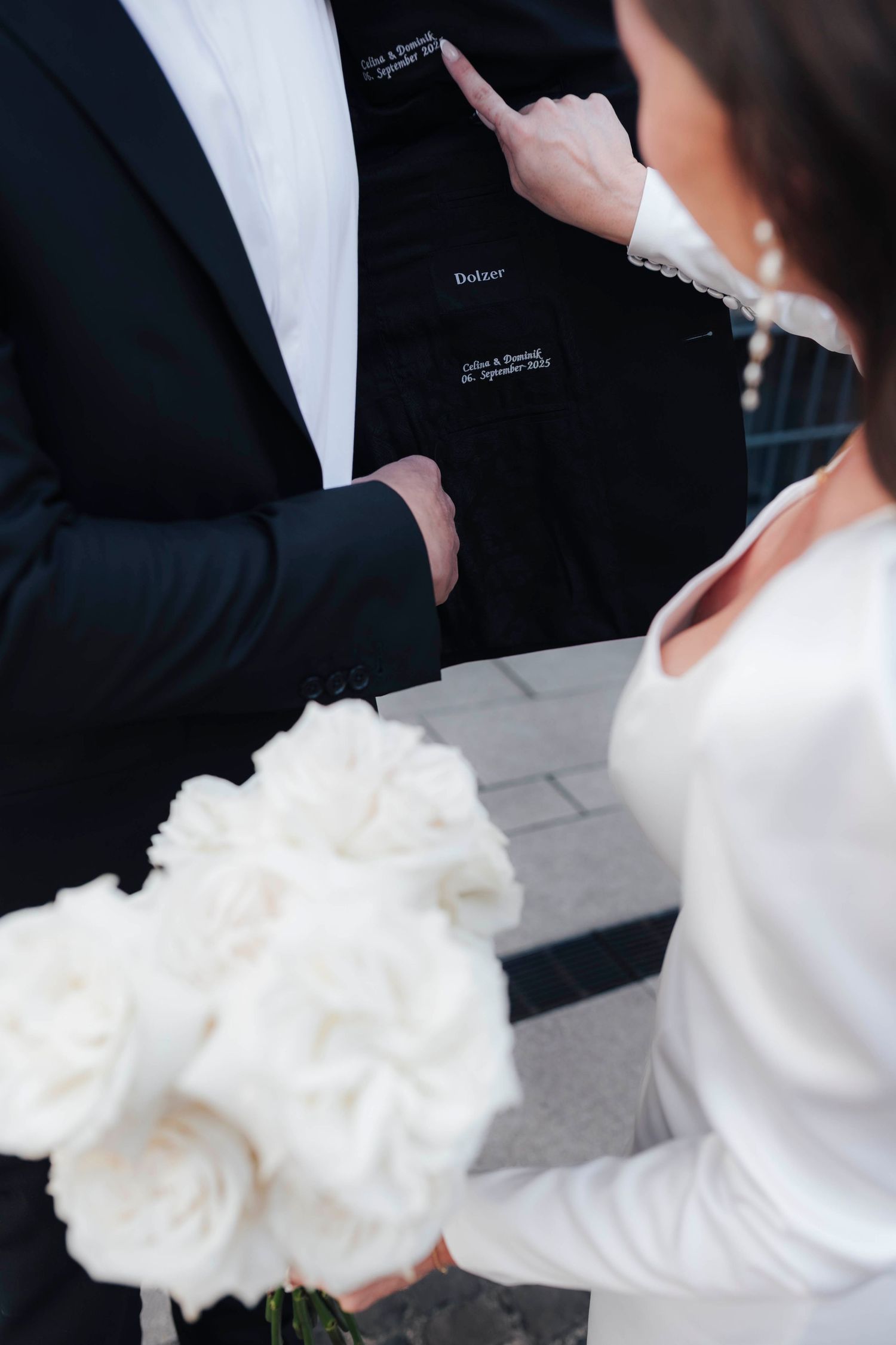Bride in white dress holding bouquet of white roses stands with groom in black suit at wedding ceremony.