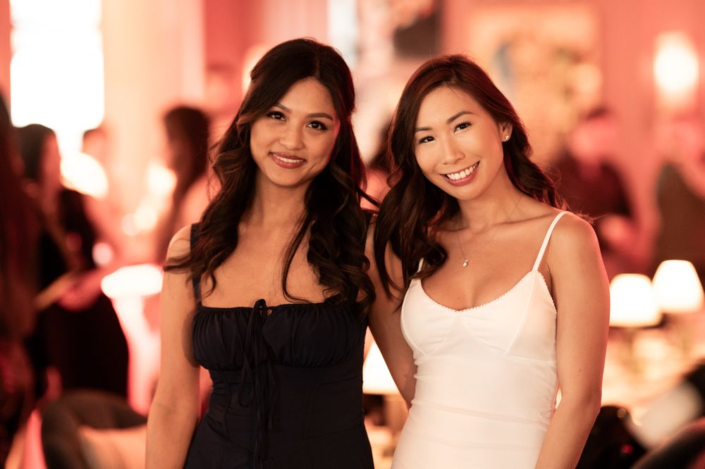 Two smiling women posing together at a social event, one in black and one in white dress.