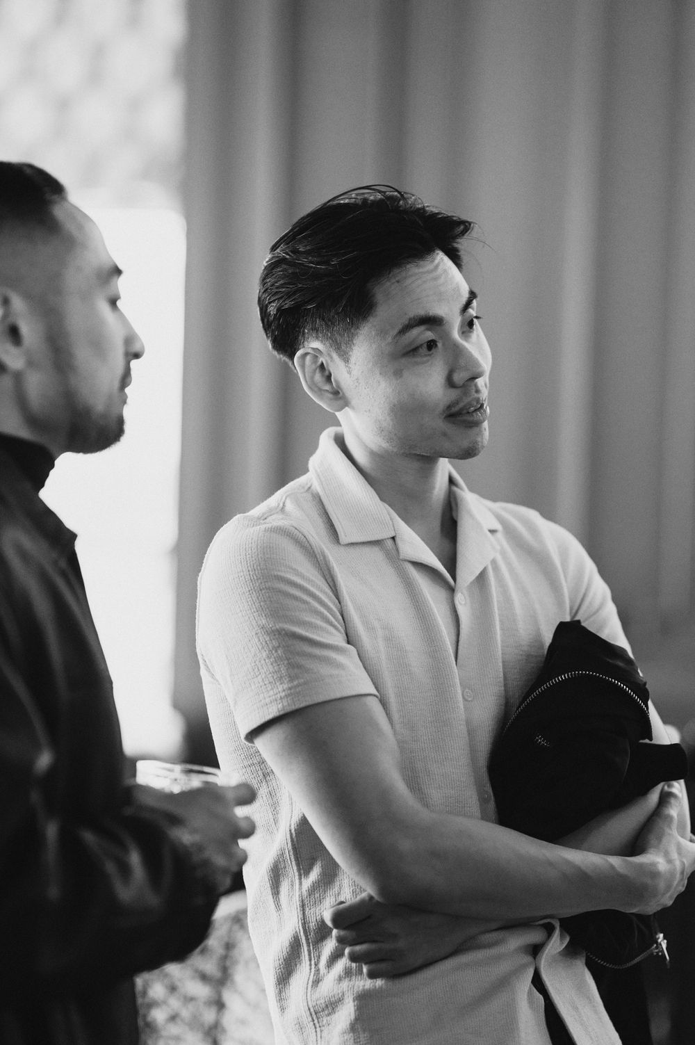 Black and white portrait of a young Asian man holding a bag at an event.