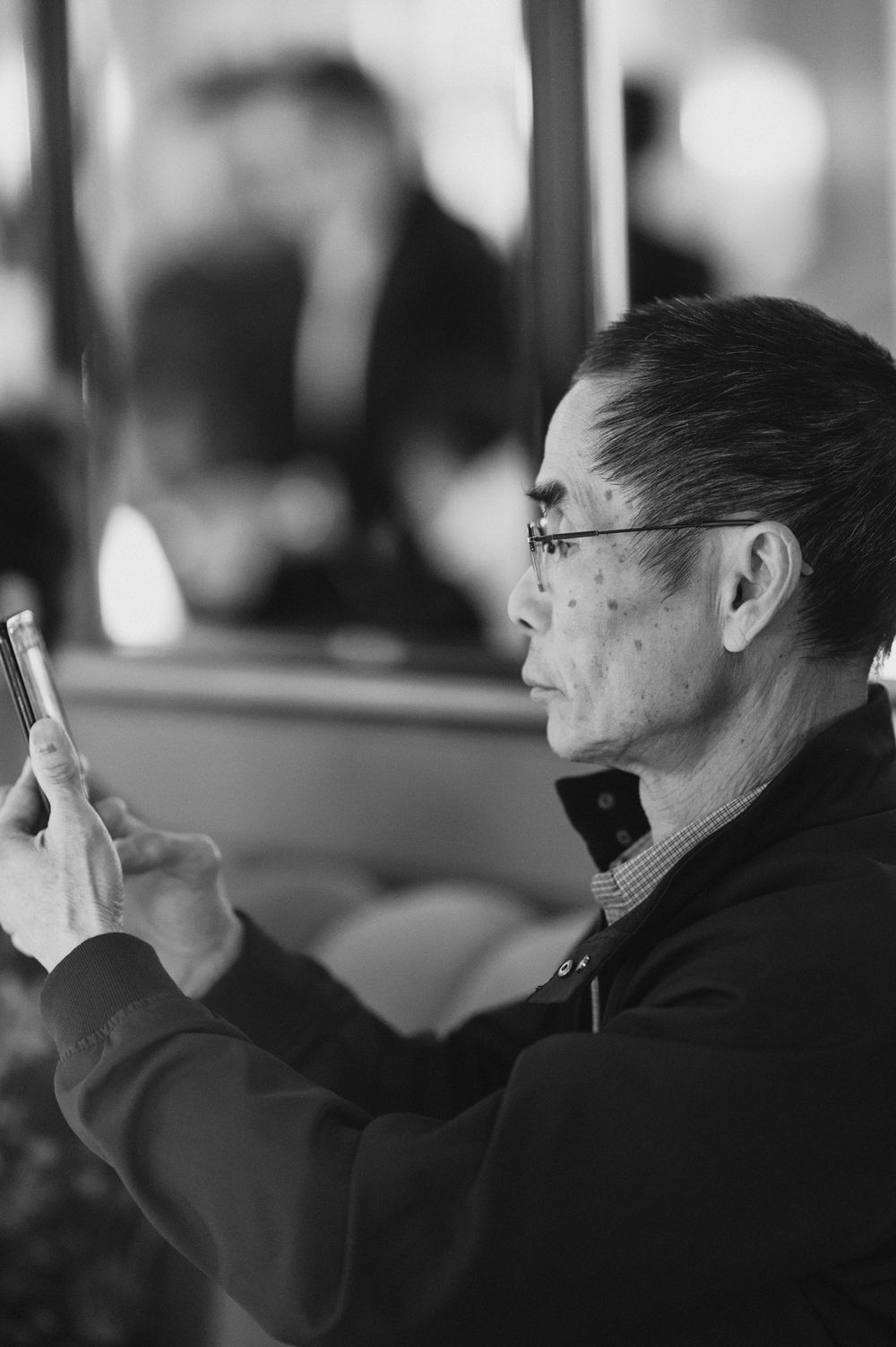 Black and white profile of an older man wearing glasses using a smartphone.
