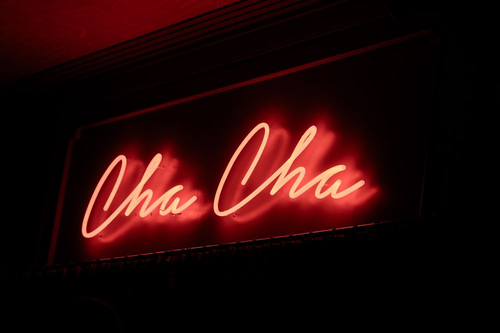 Red neon Cha Cha sign glowing in the dark at a nightclub or bar.