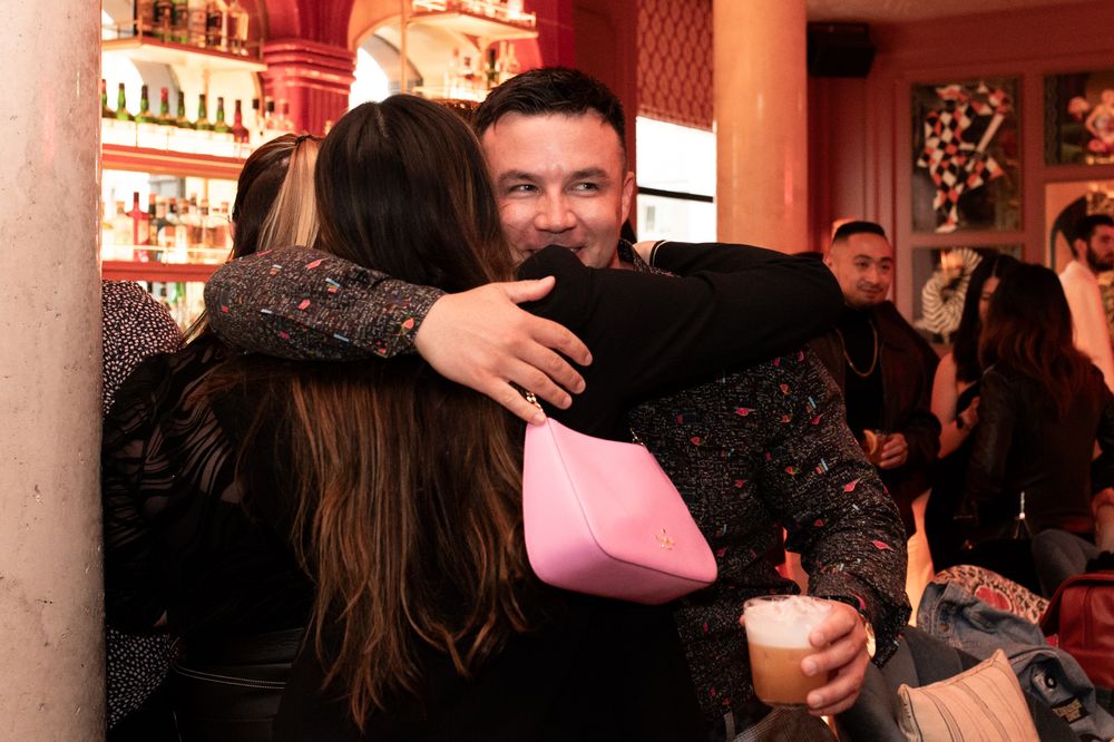 Man smiling while hugging a guest at a lively indoor social gathering event.