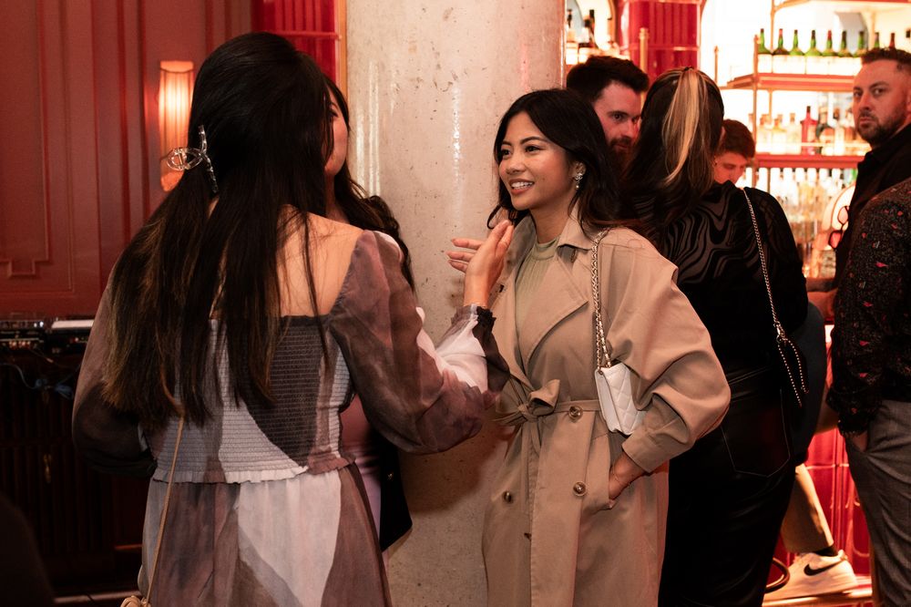 Two women in stylish outfits conversing at an upscale social gathering.