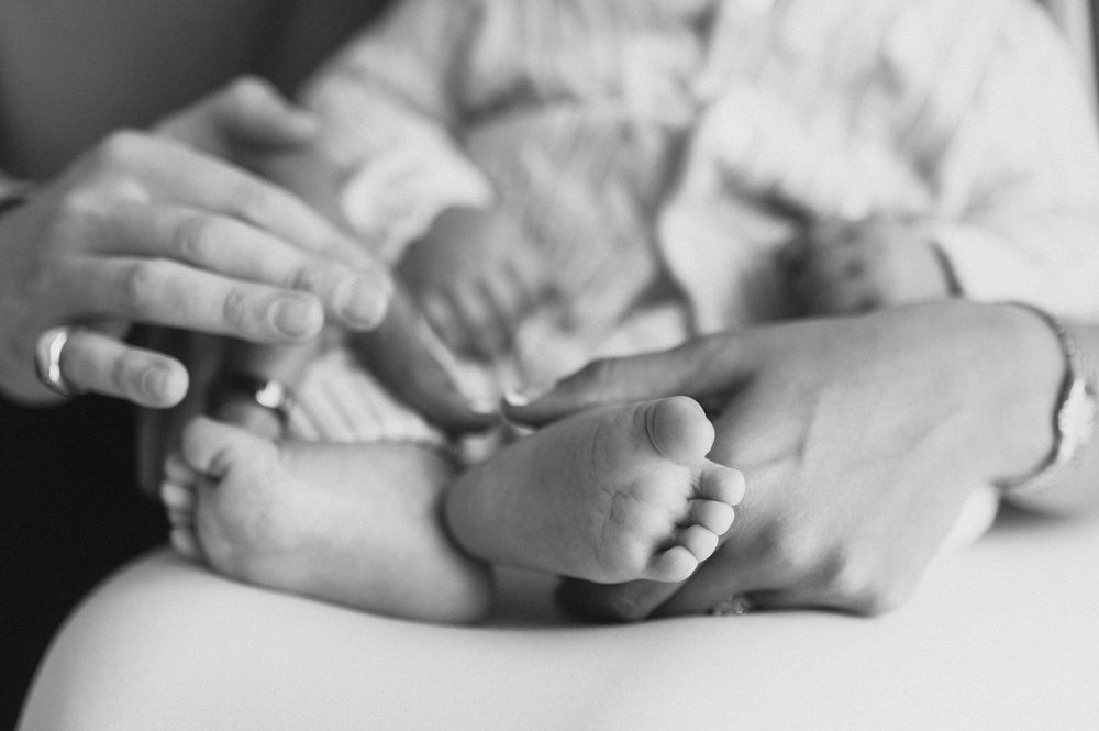Black and white photo of adult hands gently holding tiny newborn baby feet.