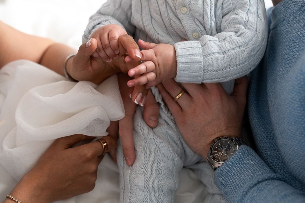 Close-up of parents and baby hands together, baby in blue knit outfit with adult watches.