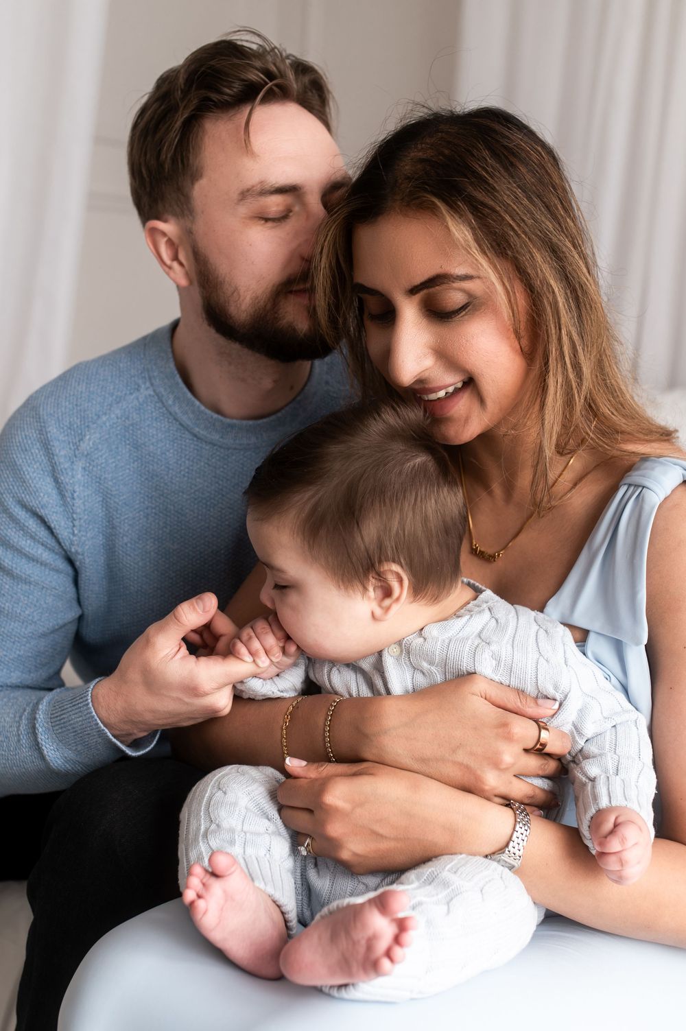 Loving father kissing mother on head while both parents cuddle their baby together tenderly.