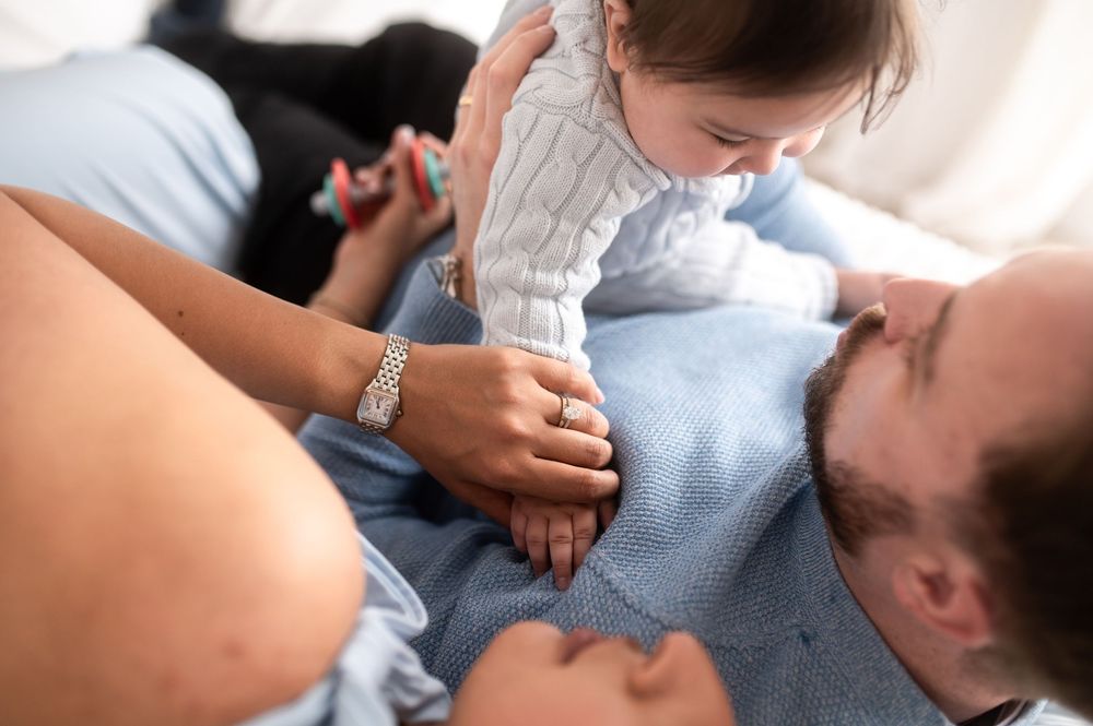 Parents lovingly hold their baby together while lying down, sharing a tender family moment.