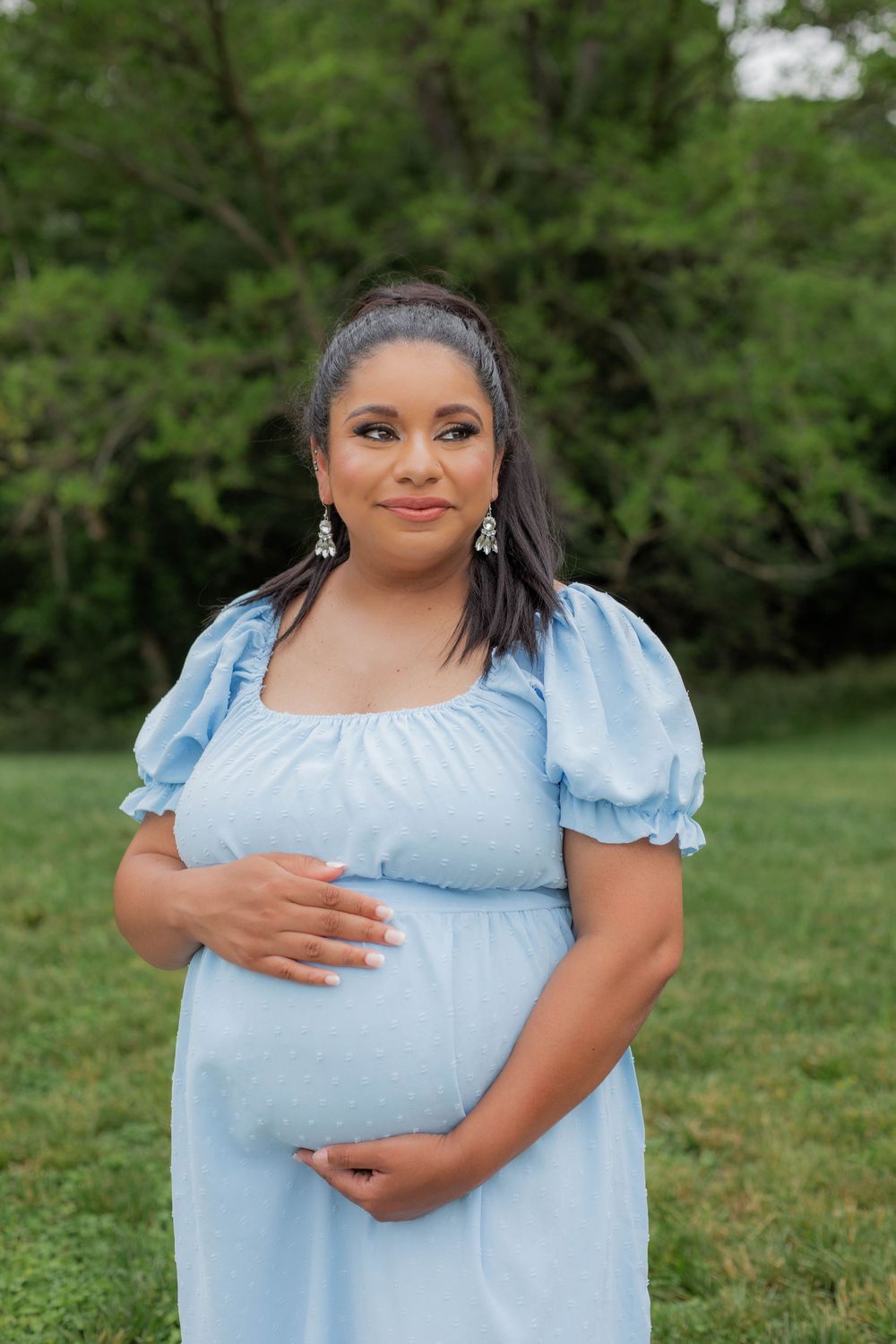 A person wearing a light blue puff sleeve dress poses outdoors against a green natural background.