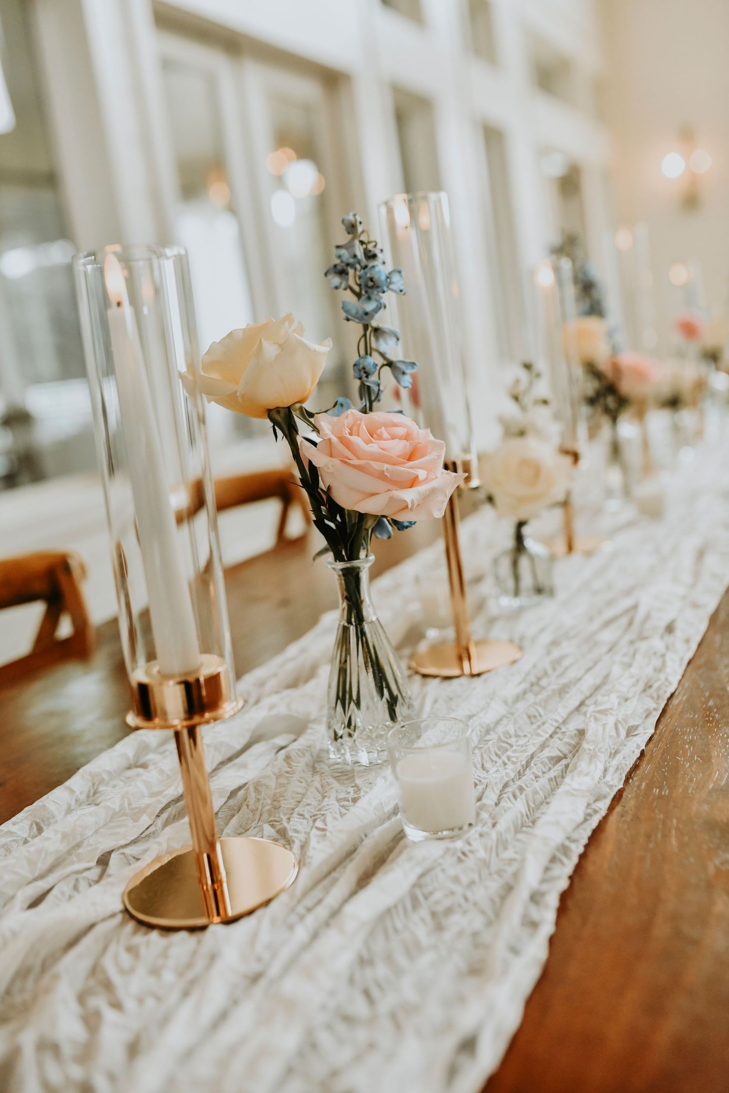 Romantic pastel wedding reception decor with tall glass candles and delicate bud vases