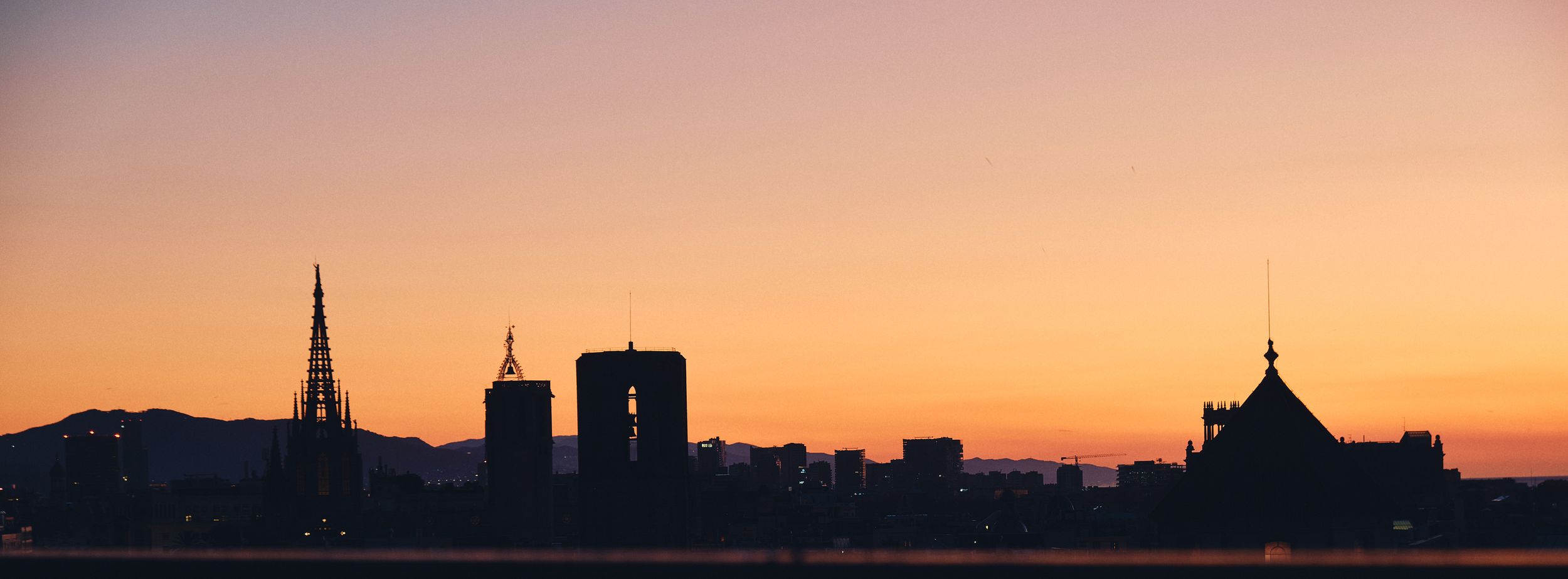 Silhouette of a city skyline with towers and domes against a vibrant orange and pink sunset sky.
