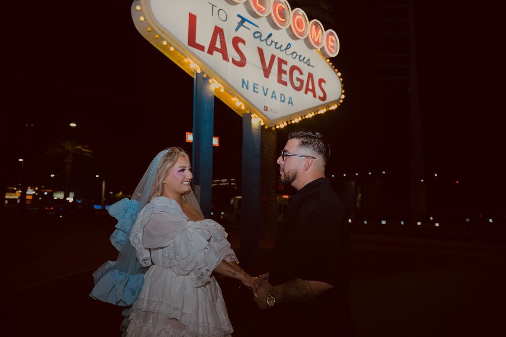 Couple holding hands in front of the iconic Welcome to Fabulous Las Vegas Nevada sign at night.