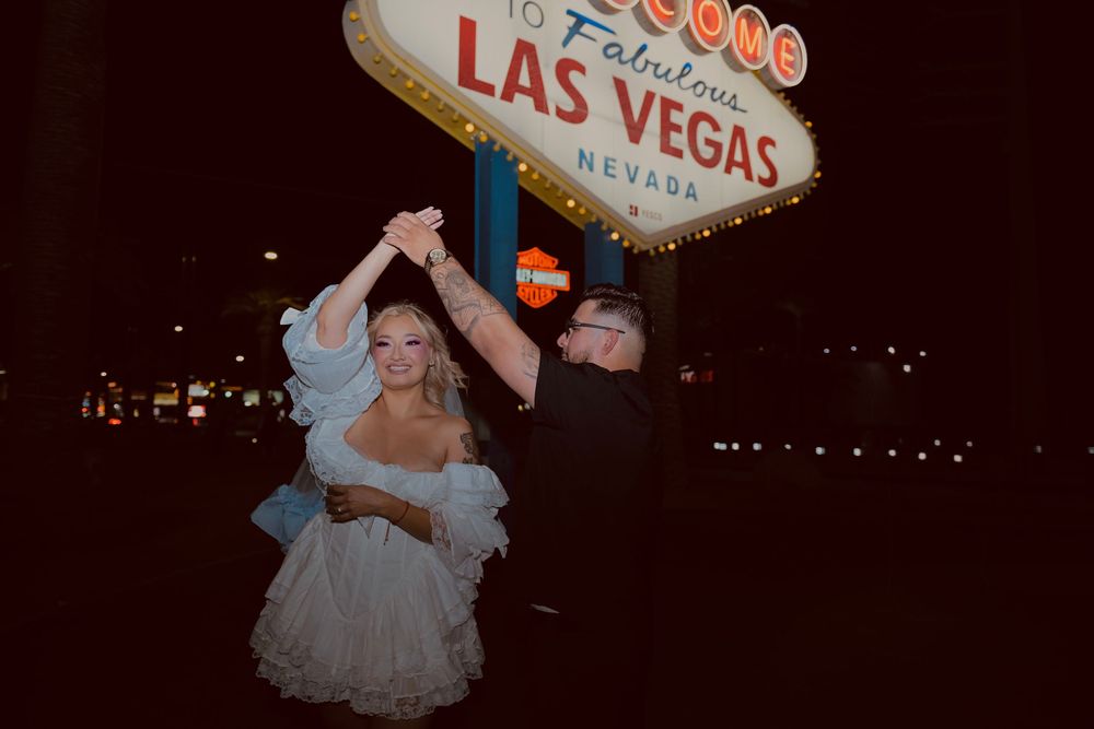 Couple dancing joyfully in front of the iconic Welcome to Fabulous Las Vegas Nevada sign at night.