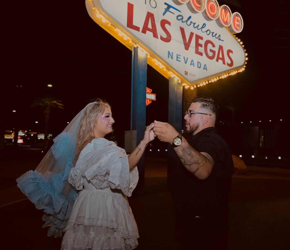 Couple celebrating wedding at iconic Welcome to Fabulous Las Vegas sign at night, bride in white gown and veil.