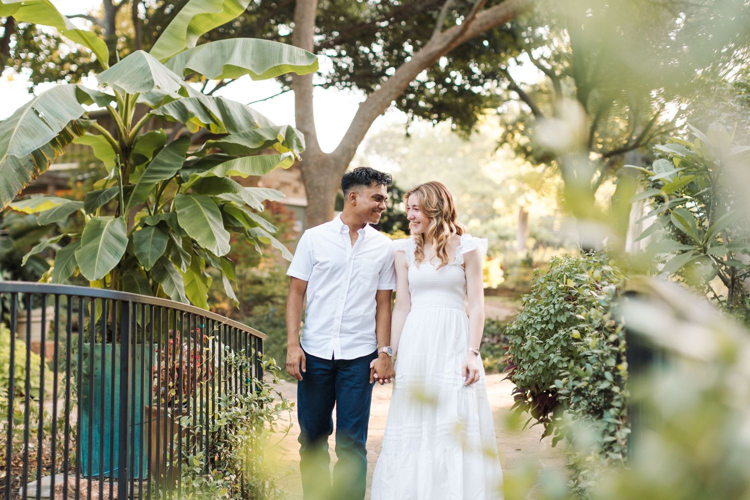 Couple holding hands and smiling at each other in a lush tropical garden setting on their wedding day.