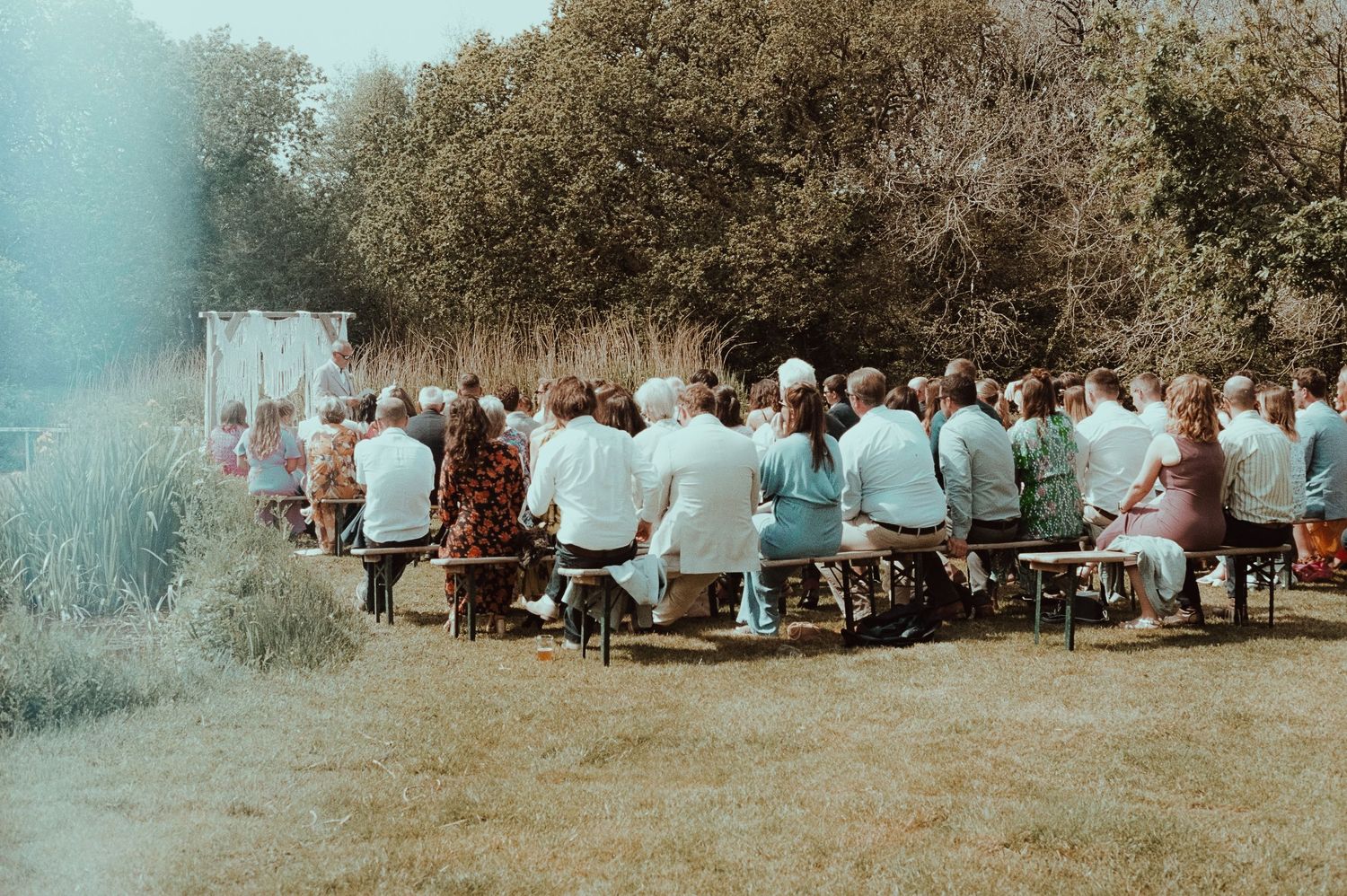 Guests seated outdoors at a rustic garden wedding ceremony surrounded by lush greenery and tall grasses.