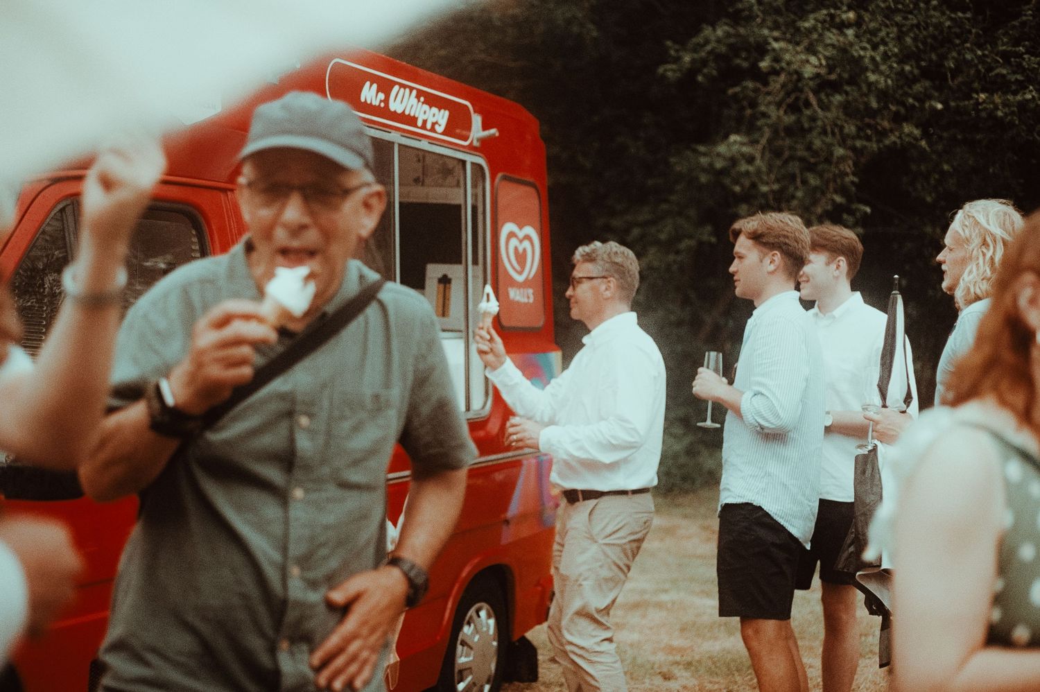 People enjoying ice cream from a red Mr Whippy van at an outdoor summer wedding.