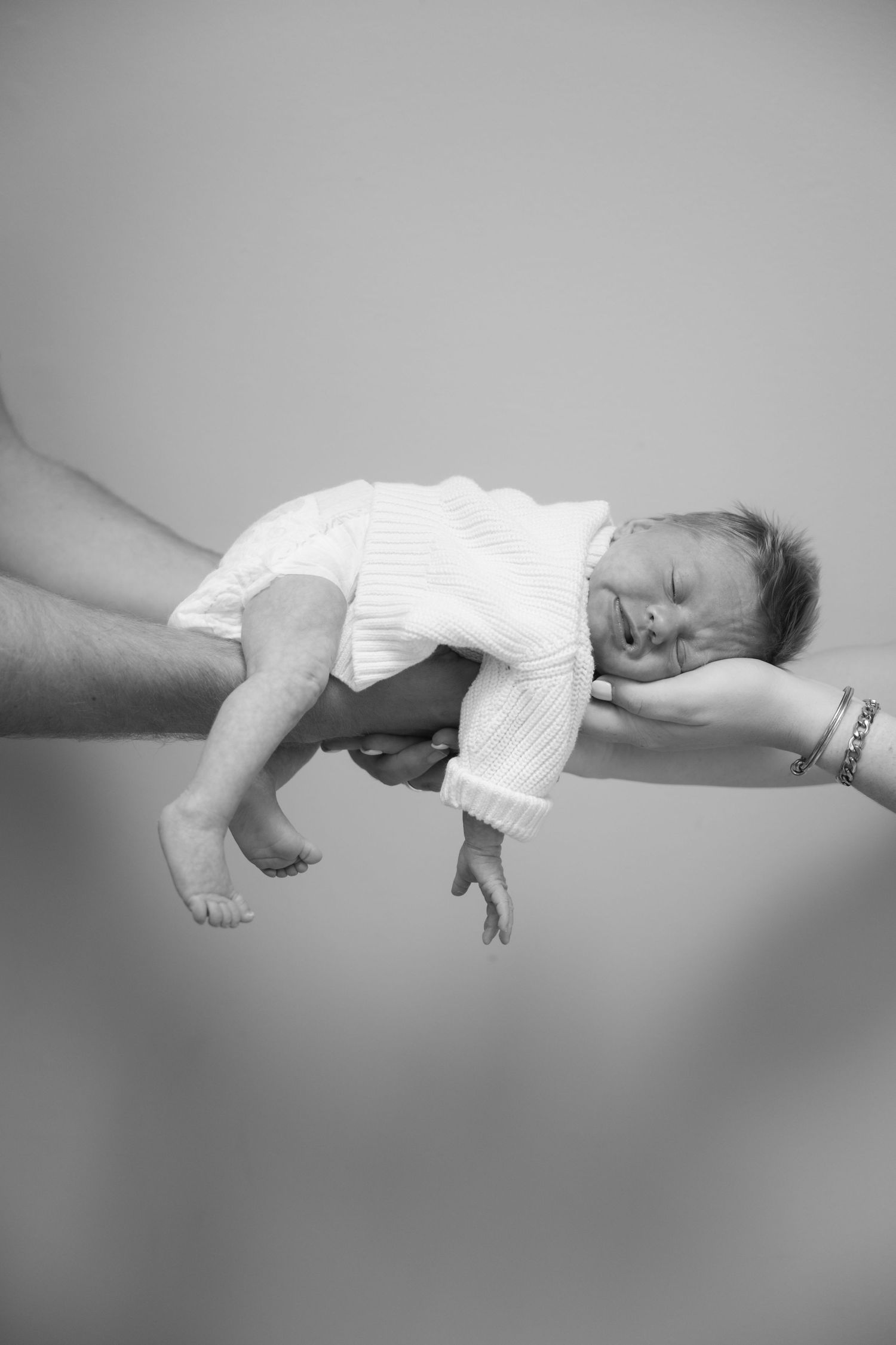 parents hands holding newborn baby on a clean backdrop during in-home lifestyle newborn session in the Twin Cities, MN.