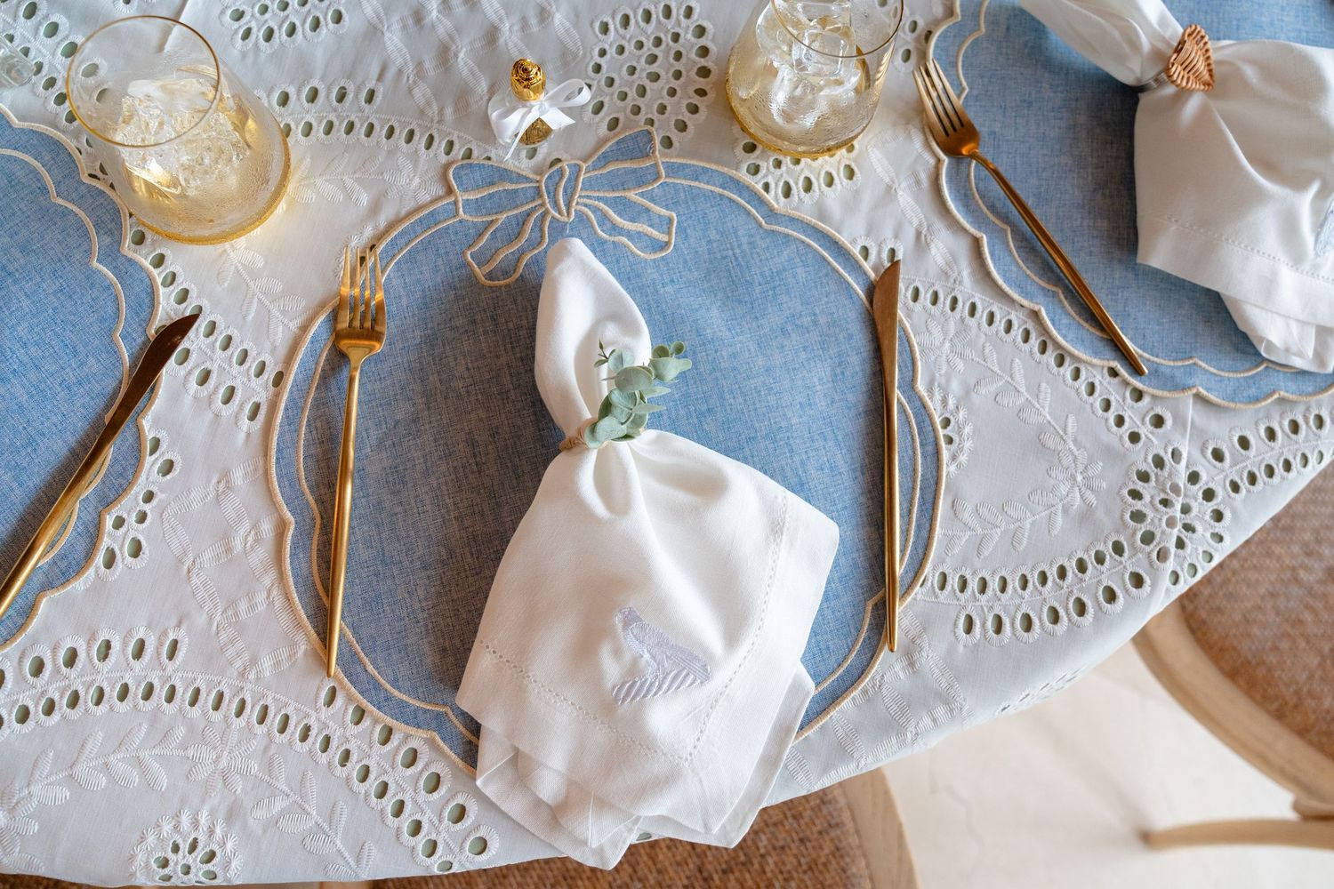Elegant blue and white table setting with gold cutlery, lace placemats, and white folded napkins on decorative plates.