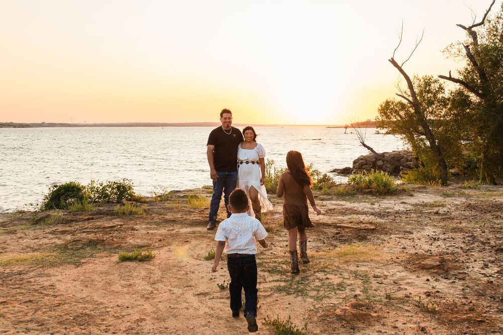 Family of four walking toward parents at golden hour sunset by a serene lakeside, children running joyfully.