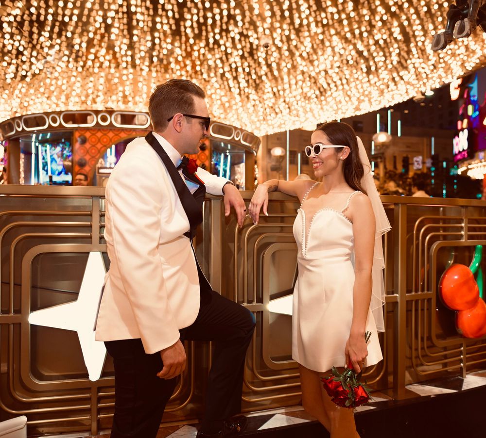 Couple in wedding attire smiling under warm string lights in a Las Vegas venue.