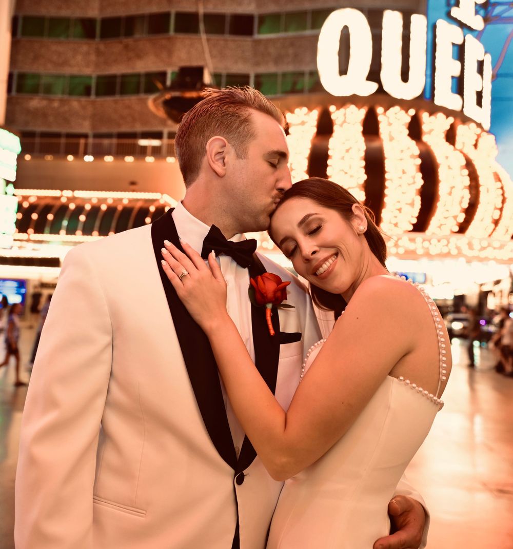 Newlywed couple in wedding attire sharing a romantic kiss on the Las Vegas Strip at night.
