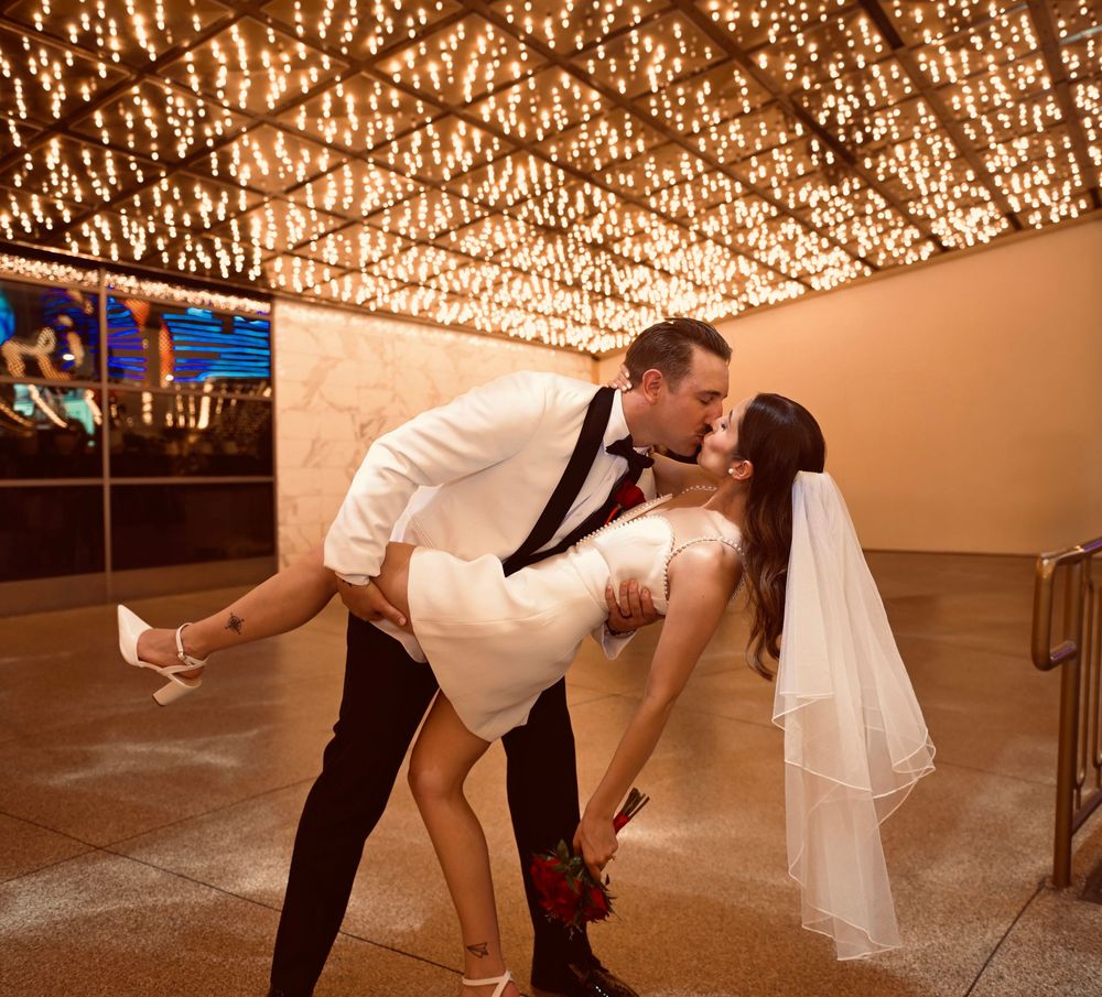 Groom dips bride for a romantic kiss under sparkling lights at a Las Vegas wedding venue.