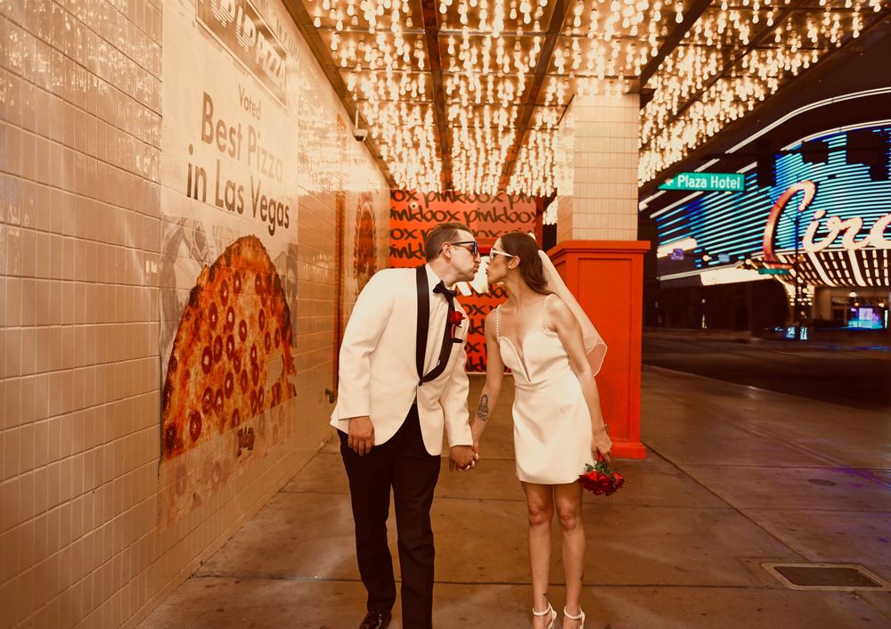 Newlywed couple kissing under glowing lights on the Las Vegas Strip in wedding attire.