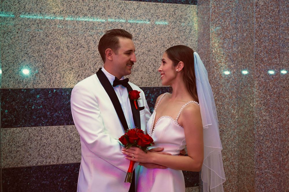 Bride and groom share a romantic moment holding red roses bouquet at their elegant wedding ceremony.