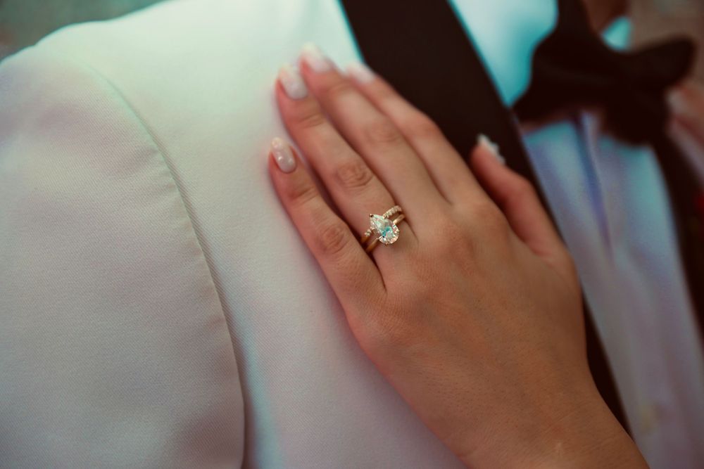 Close-up of a diamond engagement ring on a woman's finger resting on a white fabric surface.