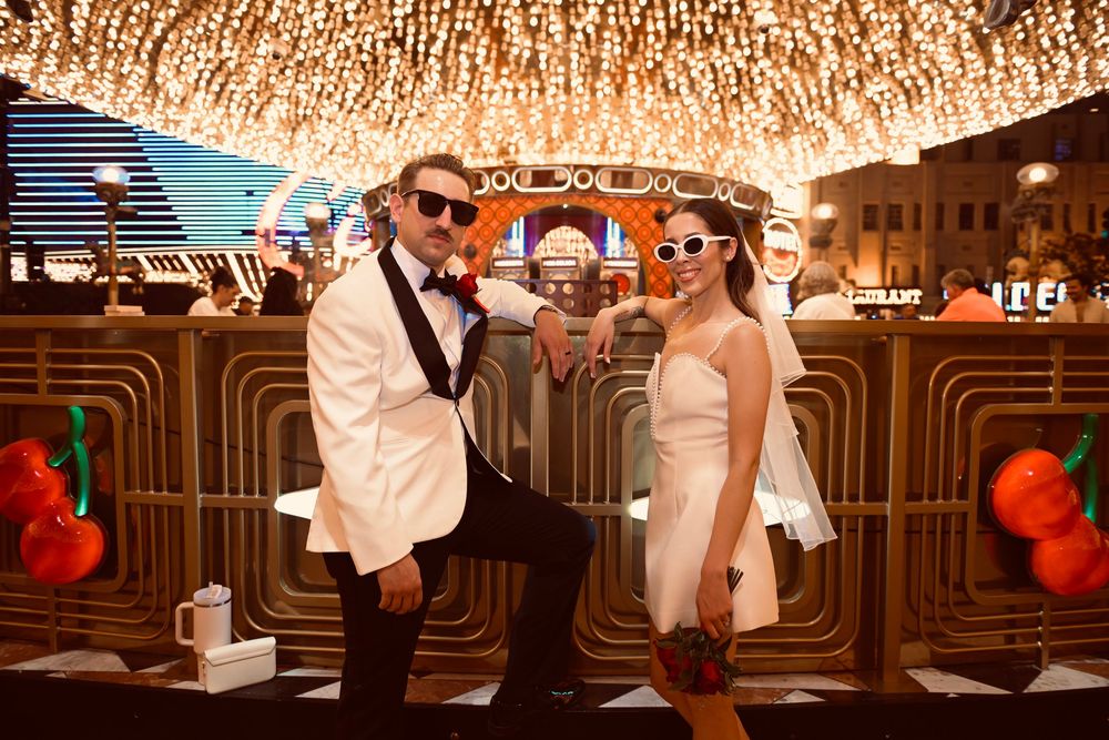 Joyful newlyweds in wedding attire posing playfully under dazzling Las Vegas lights at night.