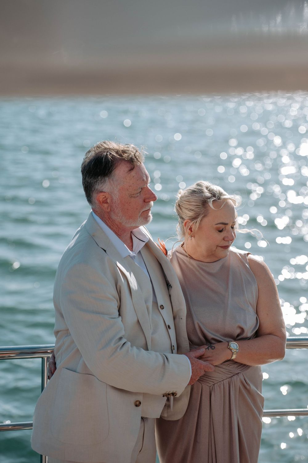 Elegant couple in formal attire embracing on a yacht deck with sparkling water in the background.