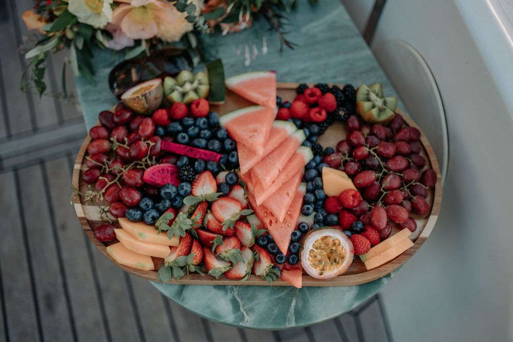 A colorful fruit platter with watermelon, strawberries, blueberries, grapes, and passion fruit arranged on a wooden board.