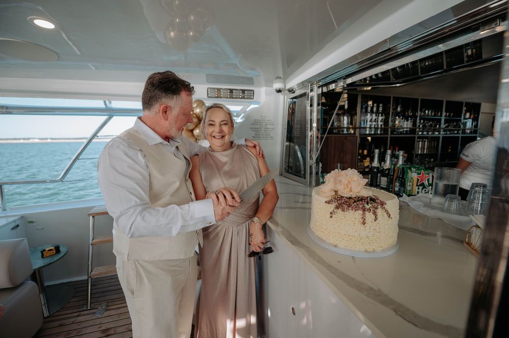Couple cutting wedding cake on a luxury yacht with a full bar backdrop and ocean views.