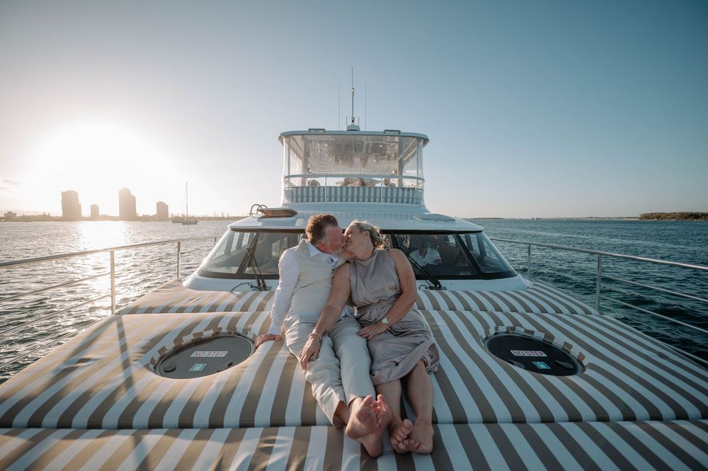 Couple kissing on luxury yacht deck at sunset with city skyline in background.